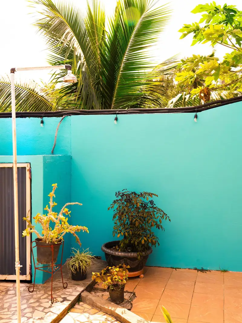 Jardin fleuri de la pension avec plantes en pot et douche extérieure sous les palmiers